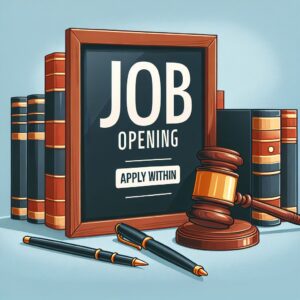 A framed sign reading “Job Opening – Apply Within” sits among law books, a judge’s gavel, and pens—symbolizing a legal job opportunity and the importance of thoughtful hiring.